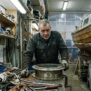 A professional yacht restoration specialist in a grit-textured workshop inspecting the locking mechanism of an AirowMarine heavy-duty 316 stainless steel porthole.