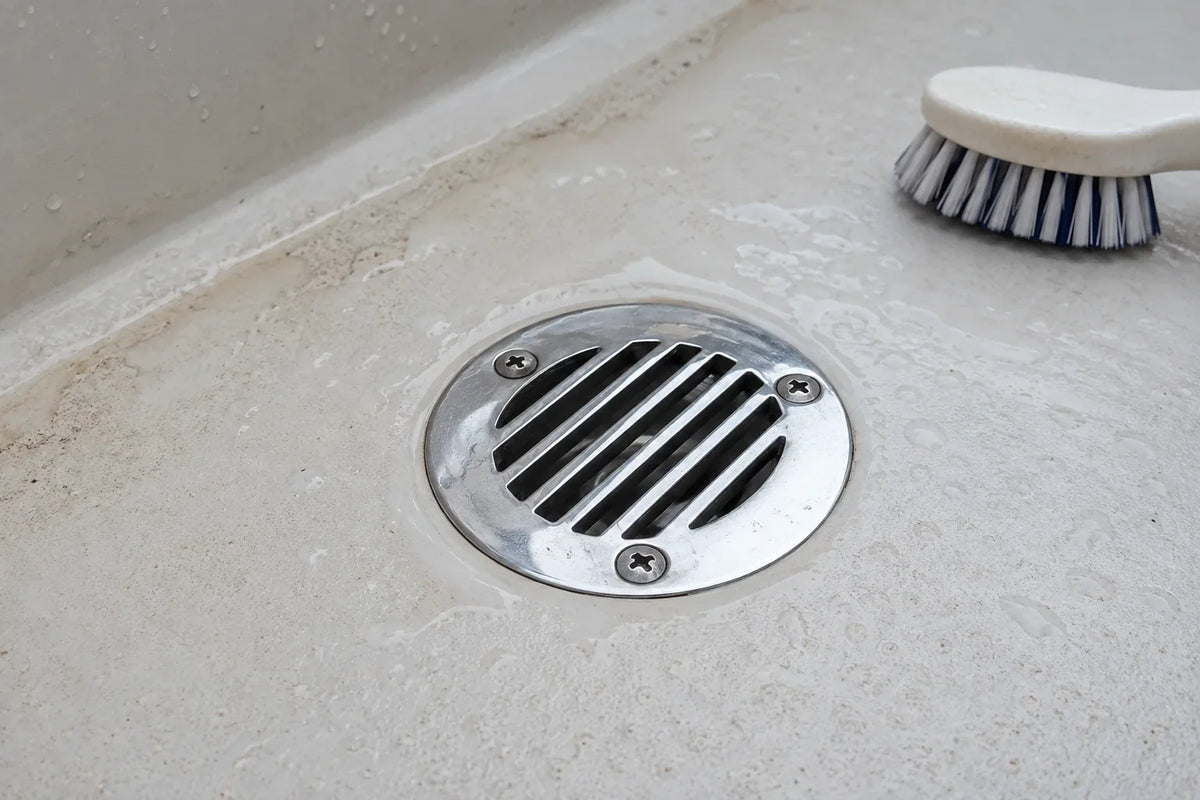 AI-generated technical illustration of a stainless boat deck drain on a wet cockpit deck beside a cleaning brush.
