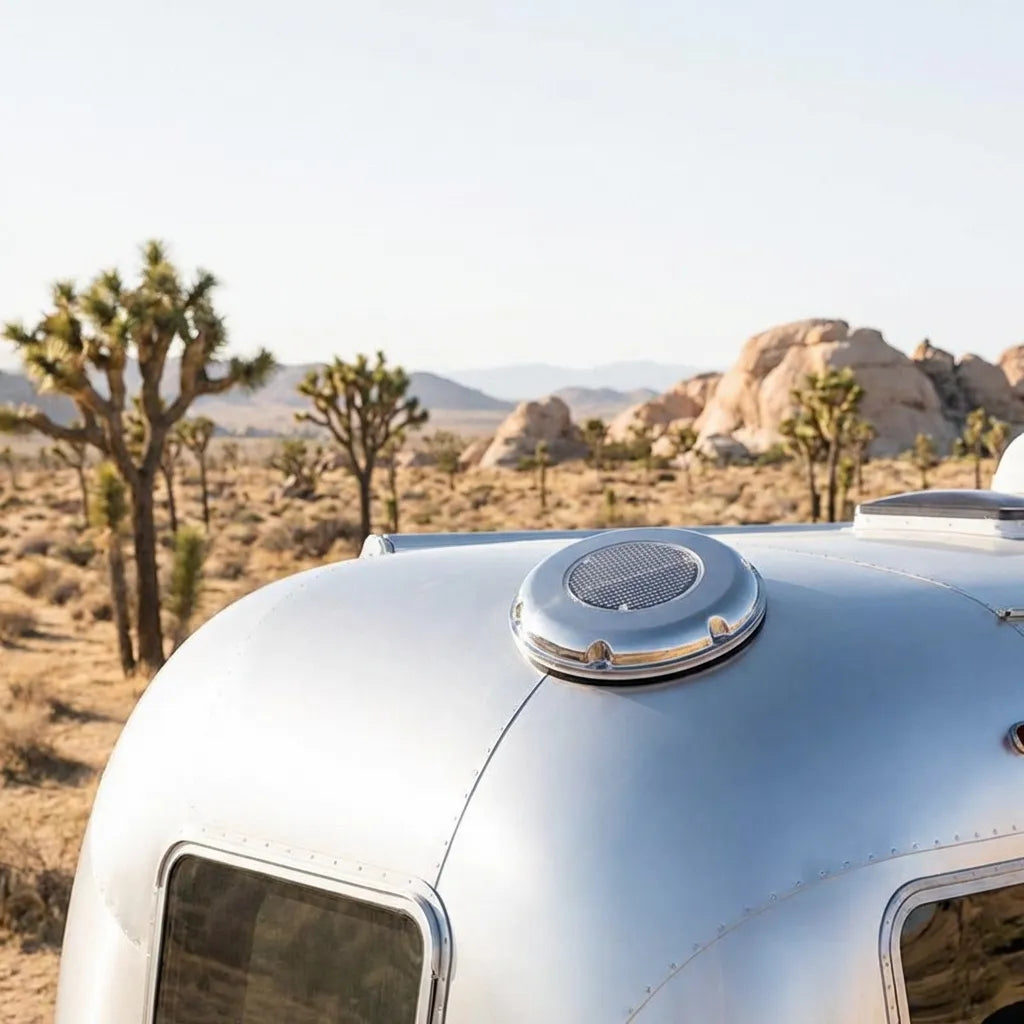 The solar ventilator mounted on the curved aluminum roof of a vintage caravan in a desert landscape.